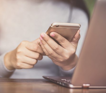 female holding smartphone getting message with confirmation making transaction on laptop computer